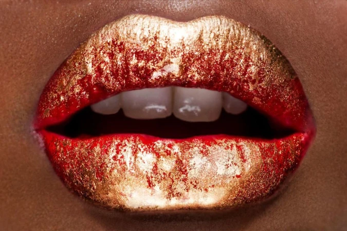 Macro view of lips adorned with red lipstick and metallic gold glitter, revealing white teeth in a slight parting