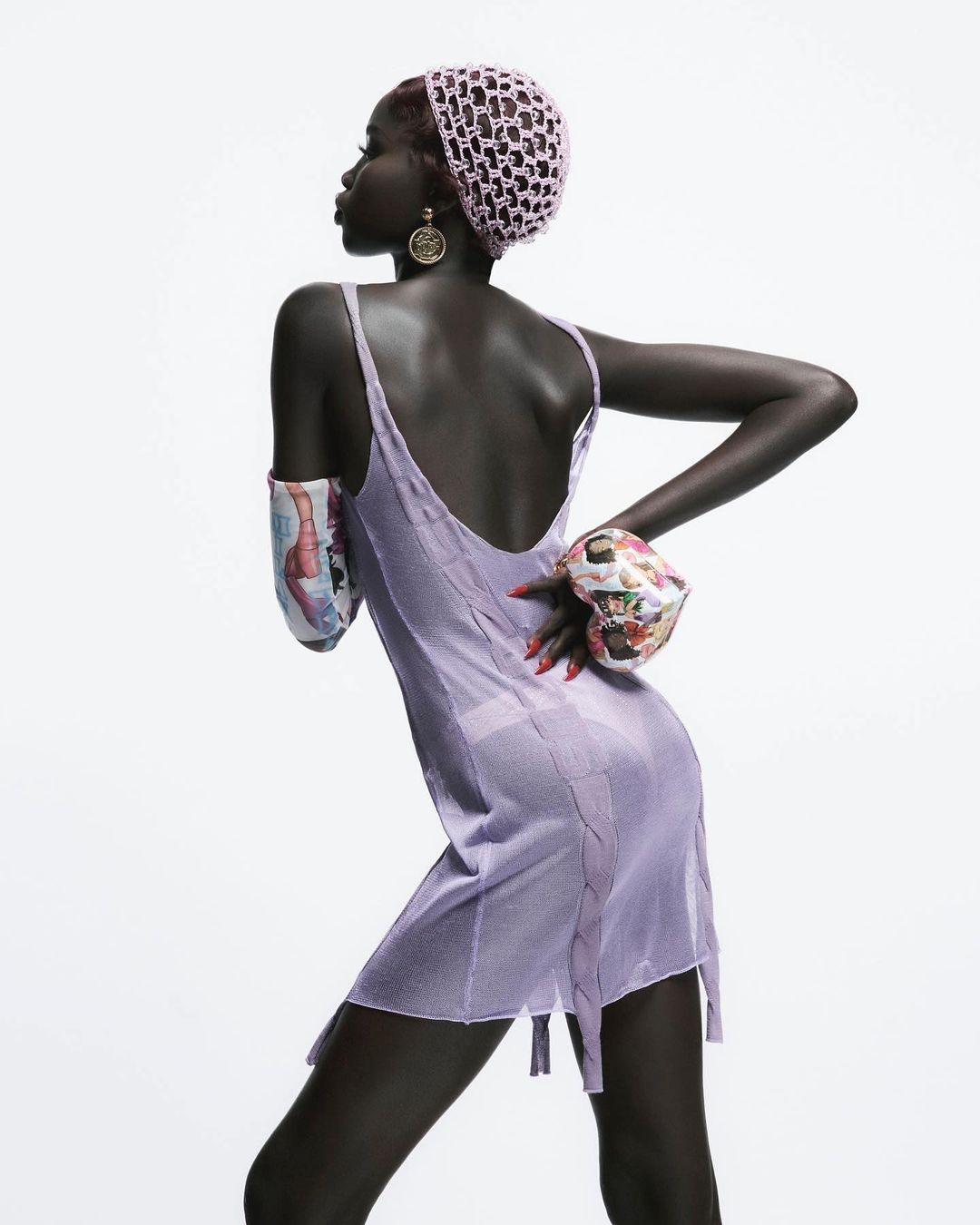 Fashion portrait of Black woman in lilac slip dress and textured head wrap posing in a white photo studio with dramatic lighting.