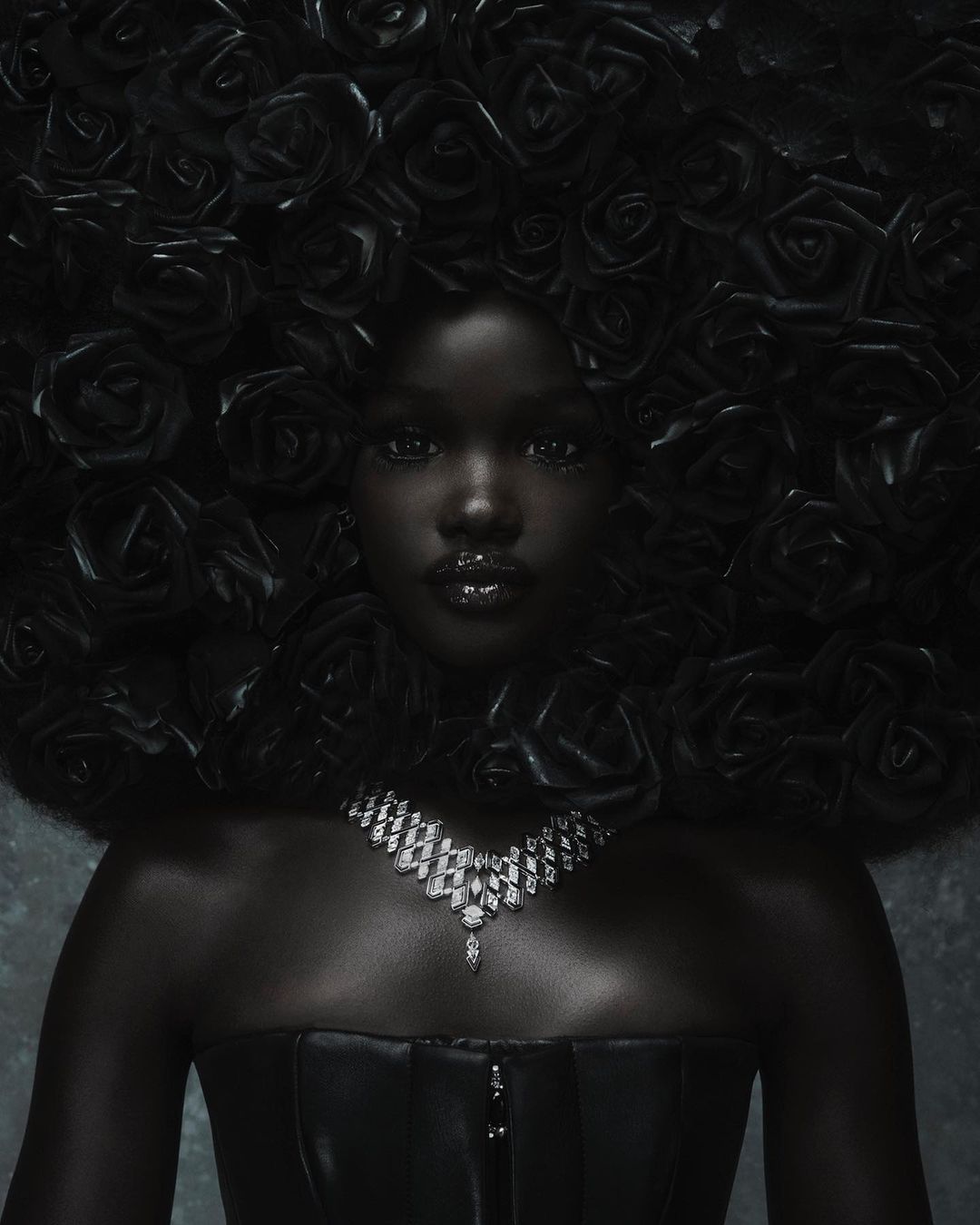 Close-up portrait of a Black woman with black rose hair adornment, wearing a black strapless top and a diamond necklace against a grey background.