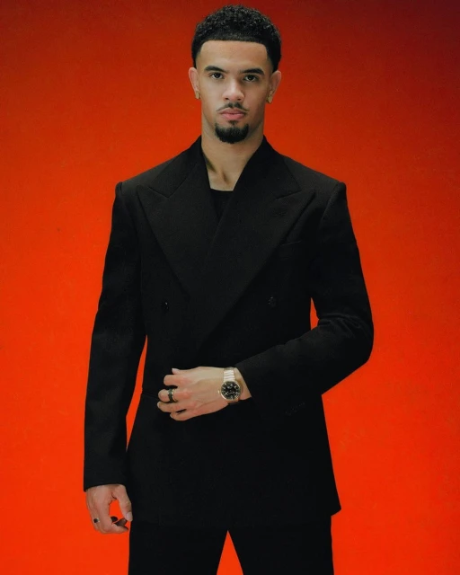 Portrait of a young man in a black suit against a vibrant orange backdrop, showcasing contemporary fashion and elegant style.