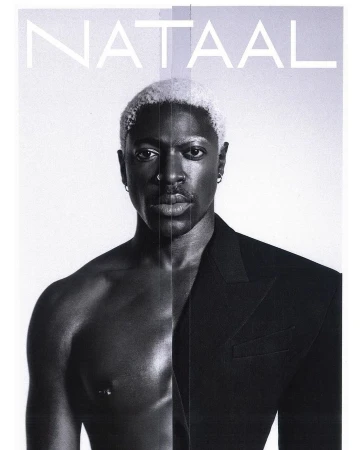 Striking black and white portrait of a shirtless Black man with platinum blonde hair wearing a blazer, set against a clean, light background.