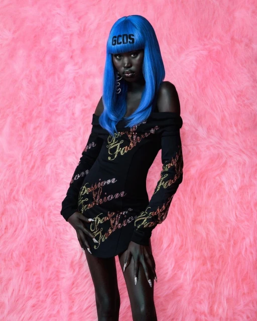 Portrait of a woman with blue hair and a black dress with 'Passion Fashion' text, against a textured pink background.