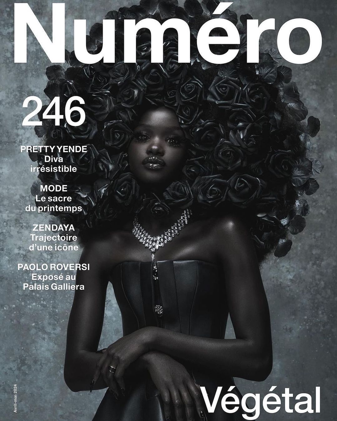 Magazine cover featuring a black model adorned with black roses, wearing a black strapless dress and a diamond necklace against a grey background.
