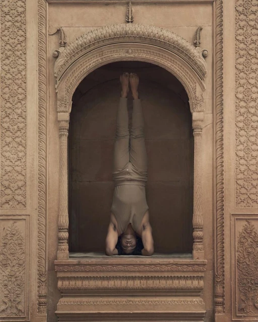 Adult male performing headstand yoga pose in stone archway. Man in a sleeveless shirt, pants and bare feet is balanced upside down.
