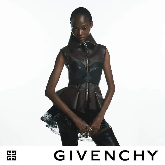 Fashion shoot of an adult African woman wearing a brown leather peplum top against a white background, jewelry on hands, and a Givenchy logo.