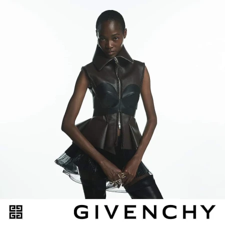 Fashion shoot of an adult African woman wearing a brown leather peplum top against a white background, jewelry on hands, and a Givenchy logo.
