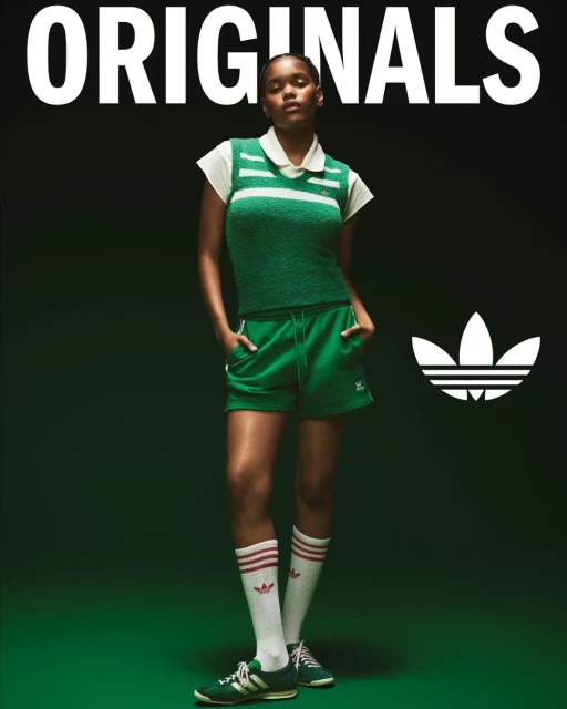 Woman in green Adidas tennis outfit stands against a dark green backdrop in a studio shot, with the Adidas logo visible.