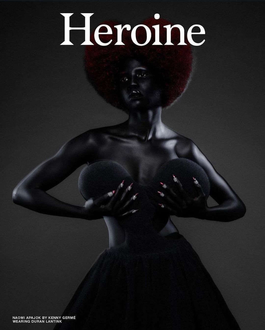 Fashion magazine cover featuring a Black female model painted in black, with a large red afro, posed against a dark gray background.