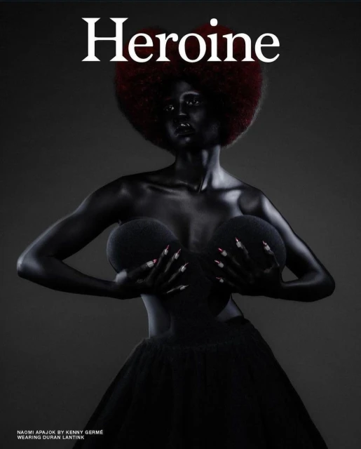 Fashion magazine cover featuring a Black female model painted in black, with a large red afro, posed against a dark gray background.