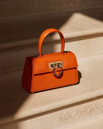 Vibrant orange leather handbag with metallic gold clasp resting on stone stairs in warm sunlight