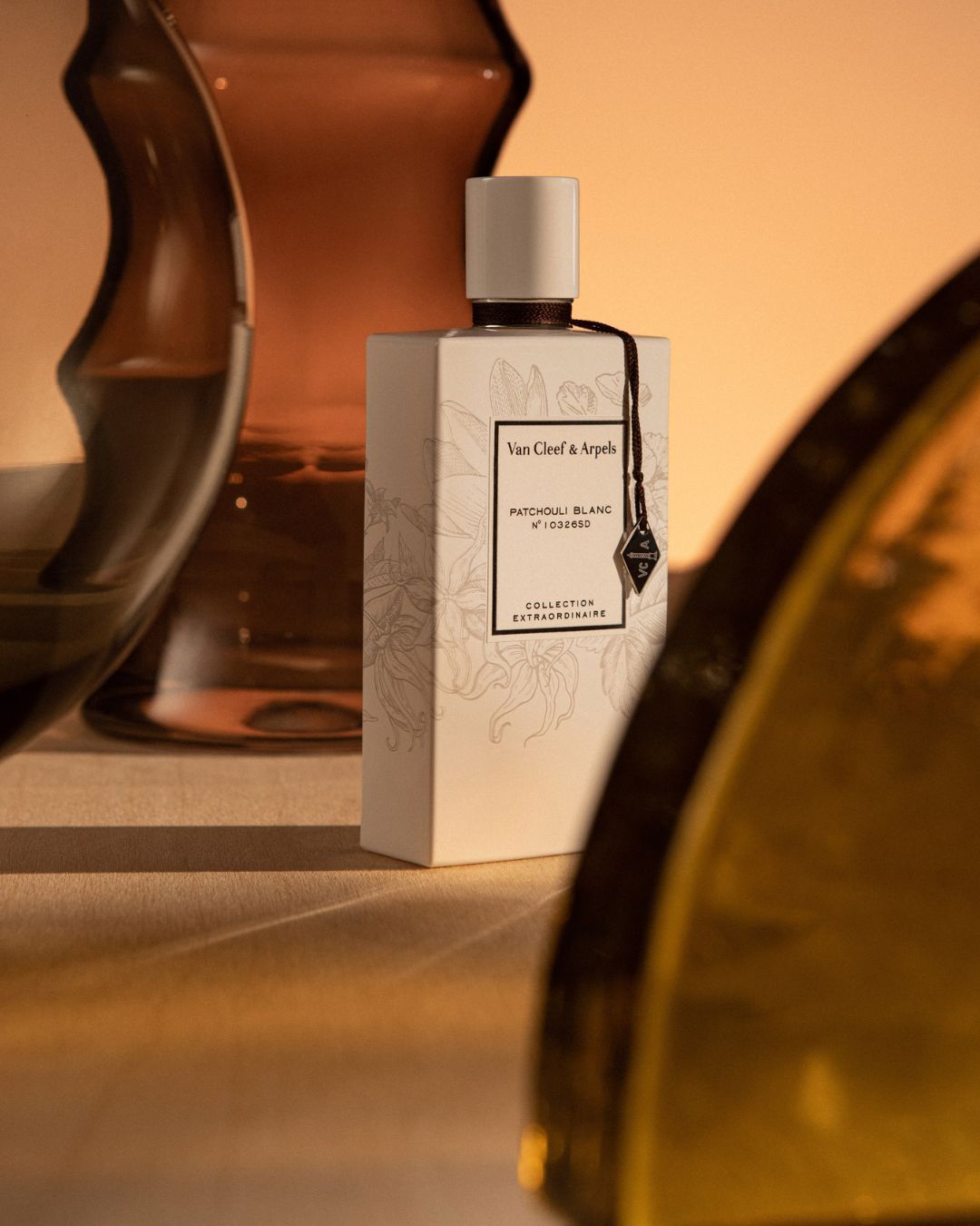 Van Cleef & Arpels perfume bottle in a studio setting, featuring soft lighting and elegant glass vase reflections.