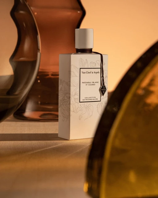 Van Cleef & Arpels perfume bottle in a studio setting, featuring soft lighting and elegant glass vase reflections.
