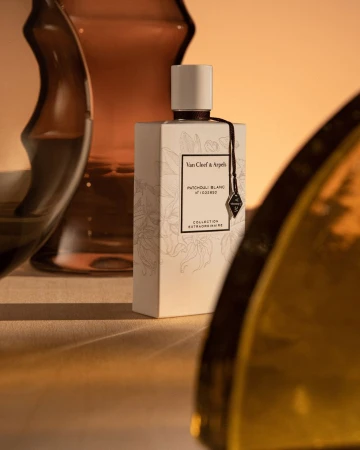 Van Cleef & Arpels perfume bottle in a studio setting, featuring soft lighting and elegant glass vase reflections.