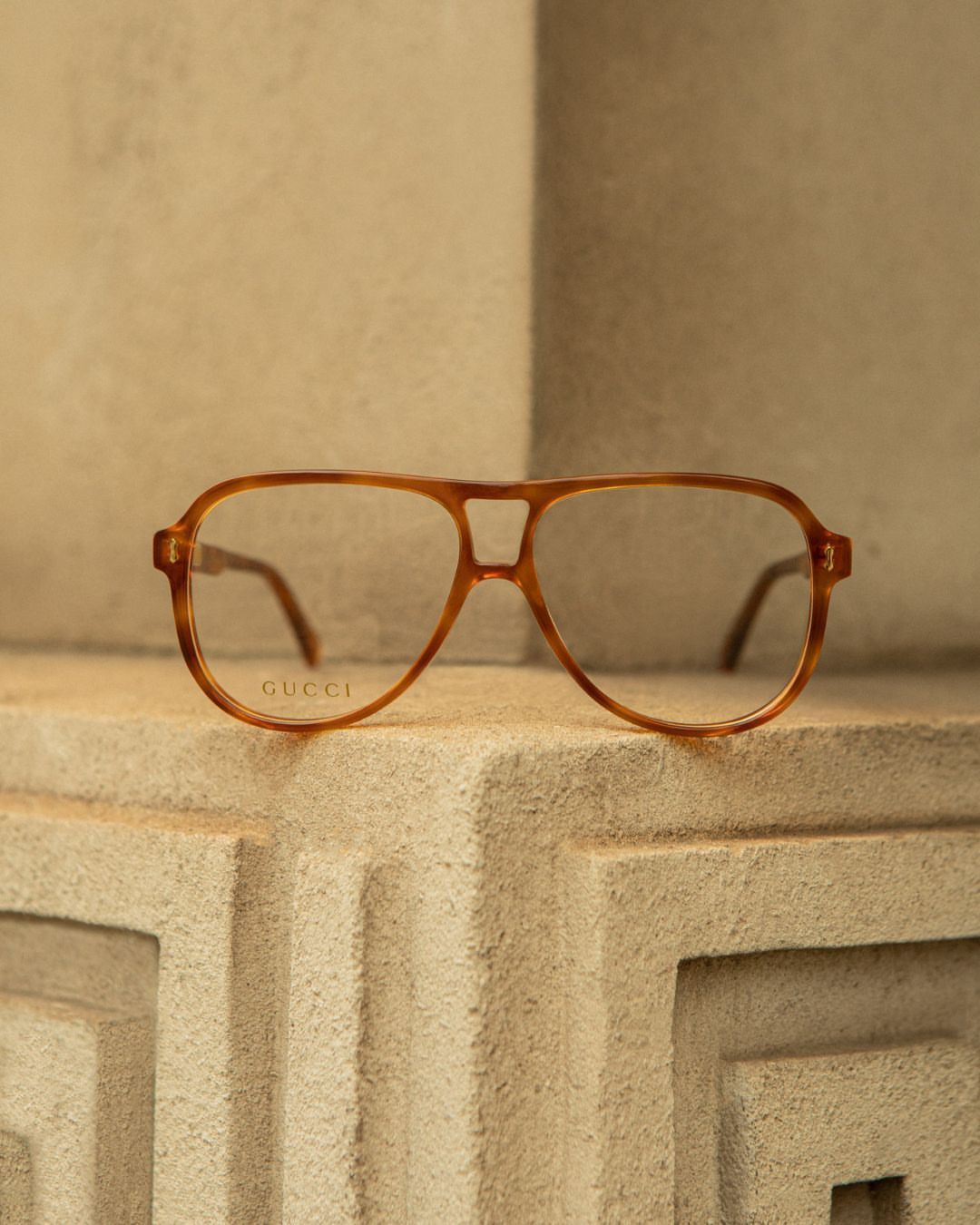Close-up shot of a pair of aviator-style eyeglasses from Gucci with a light brown frame resting on a textured stone surface.