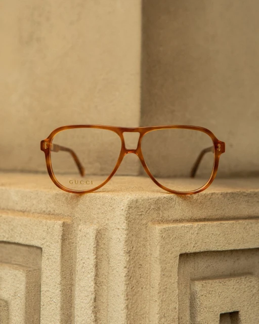 Close-up shot of a pair of aviator-style eyeglasses from Gucci with a light brown frame resting on a textured stone surface.