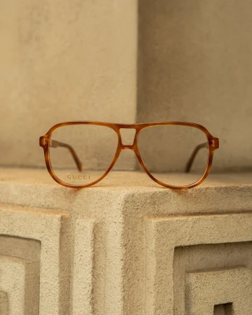 Close-up shot of a pair of aviator-style eyeglasses from Gucci with a light brown frame resting on a textured stone surface.