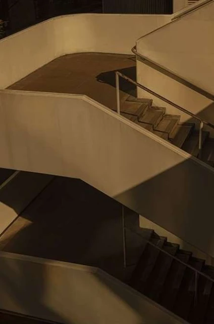 Architectural shot of a stark white staircase winding upwards in a modern urban setting, casting sharp shadows in the dim light.