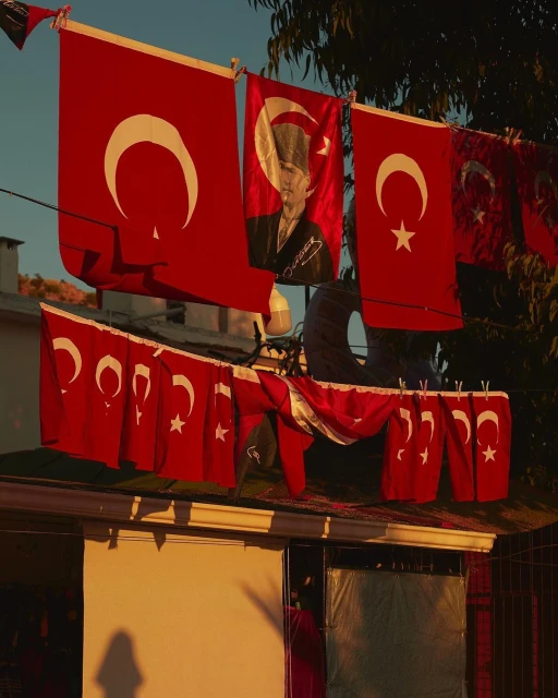Display of Turkish flags, some featuring Mustafa Kemal Atatürk, hanging outdoors on a line above a building during daytime.