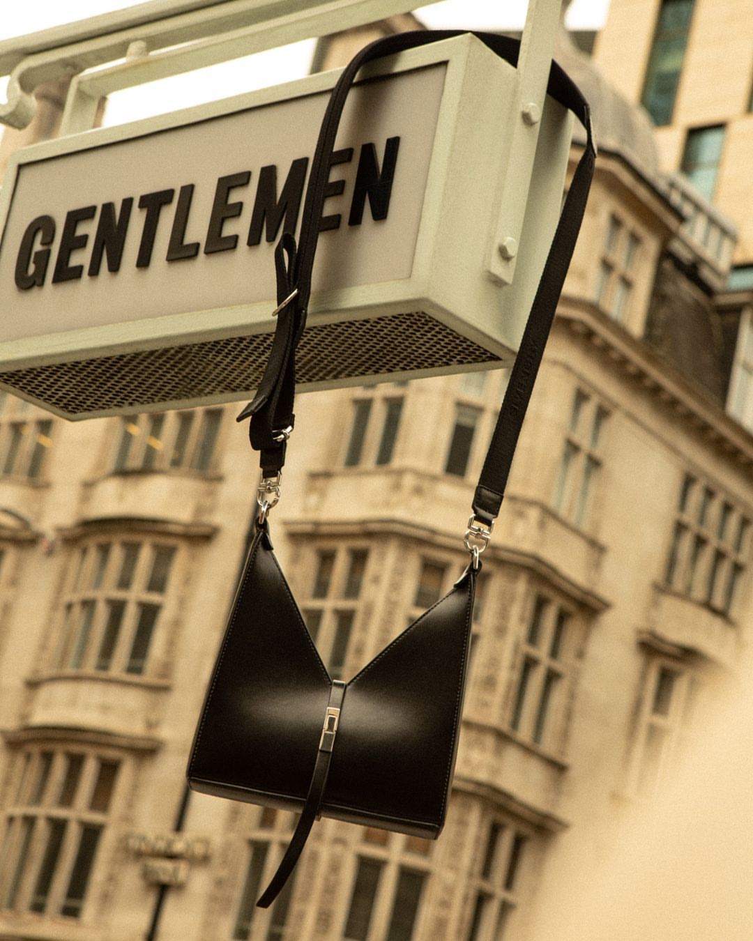 Black leather crossbody bag with silver hardware and shoulder strap against an out-of-focus urban background.