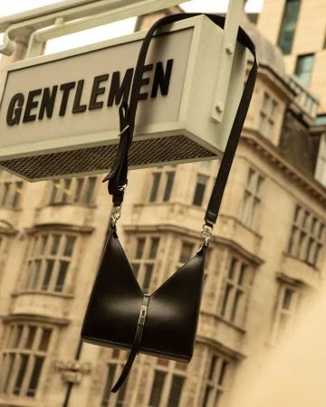 Black leather crossbody bag with silver hardware and shoulder strap against an out-of-focus urban background.