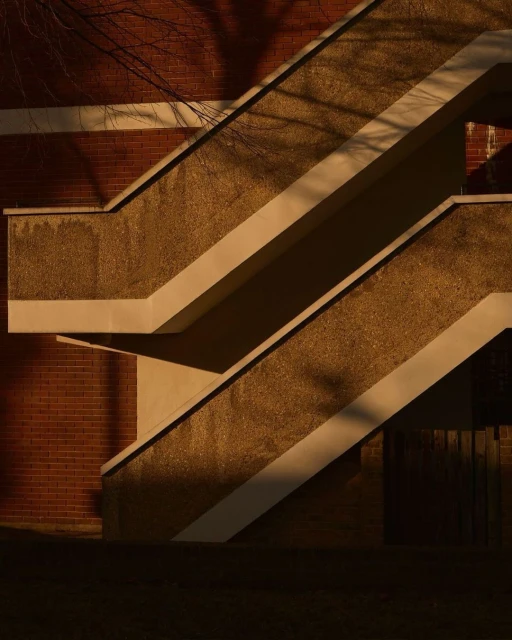 Exterior shot of a modern concrete staircase with shadows falling on the stairs and brick wall during daytime, creating architectural image.