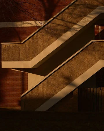 Exterior shot of a modern concrete staircase with shadows falling on the stairs and brick wall during daytime, creating architectural image.