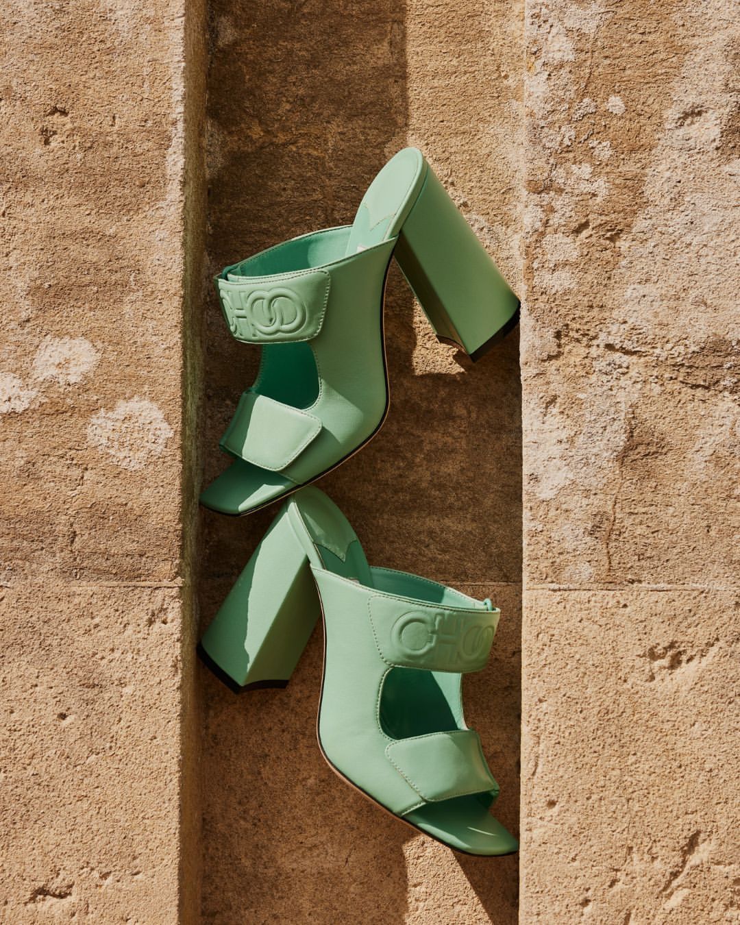 Pair of light green CHLOE sandals are displayed on a weathered stone ledge in a close-up shot, creating a high-fashion footwear image.