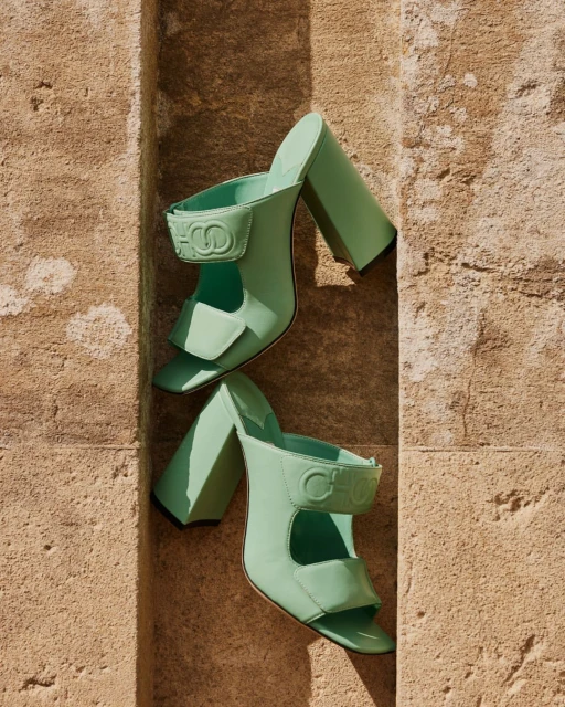 Pair of light green CHLOE sandals are displayed on a weathered stone ledge in a close-up shot, creating a high-fashion footwear image.