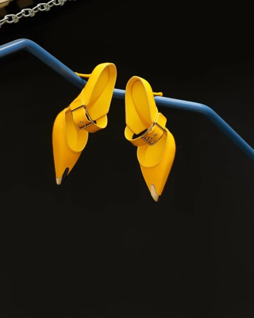 Bright yellow heeled buckle shoes rest on a blue bar in a studio, fashion-forward and eye-catching against the dark backdrop.