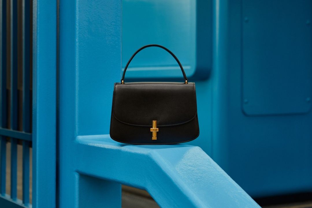 Black leather handbag with gold hardware on a bright blue architectural structure, showcasing fashion accessory and vibrant color contrast.