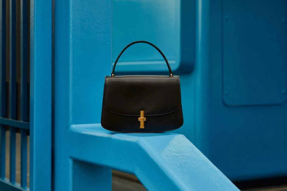 Black leather handbag with gold hardware on a bright blue architectural structure, showcasing fashion accessory and vibrant color contrast.