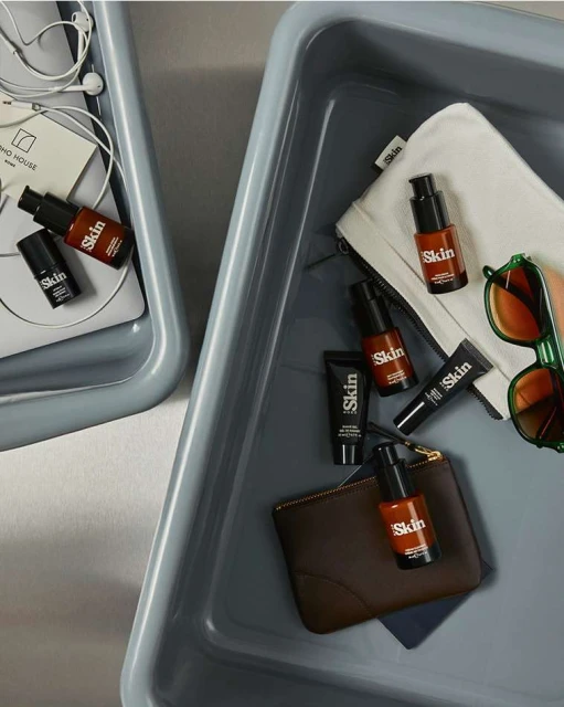 Cosmetics in gray trays includes skincare bottles, tubes, wallets, headphones, and sunglasses. Beauty and personal care products.