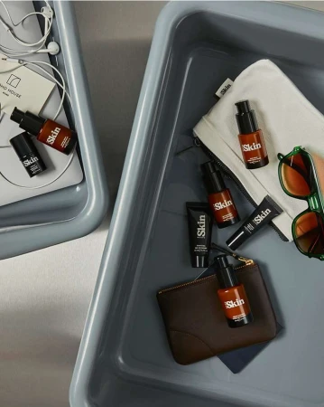 Cosmetics in gray trays includes skincare bottles, tubes, wallets, headphones, and sunglasses. Beauty and personal care products.
