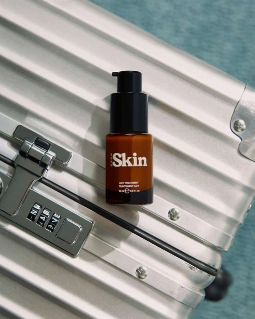 Brown glass bottle of daily treatment skin serum with black pump top displayed on a striped silver suitcase with a combination lock.