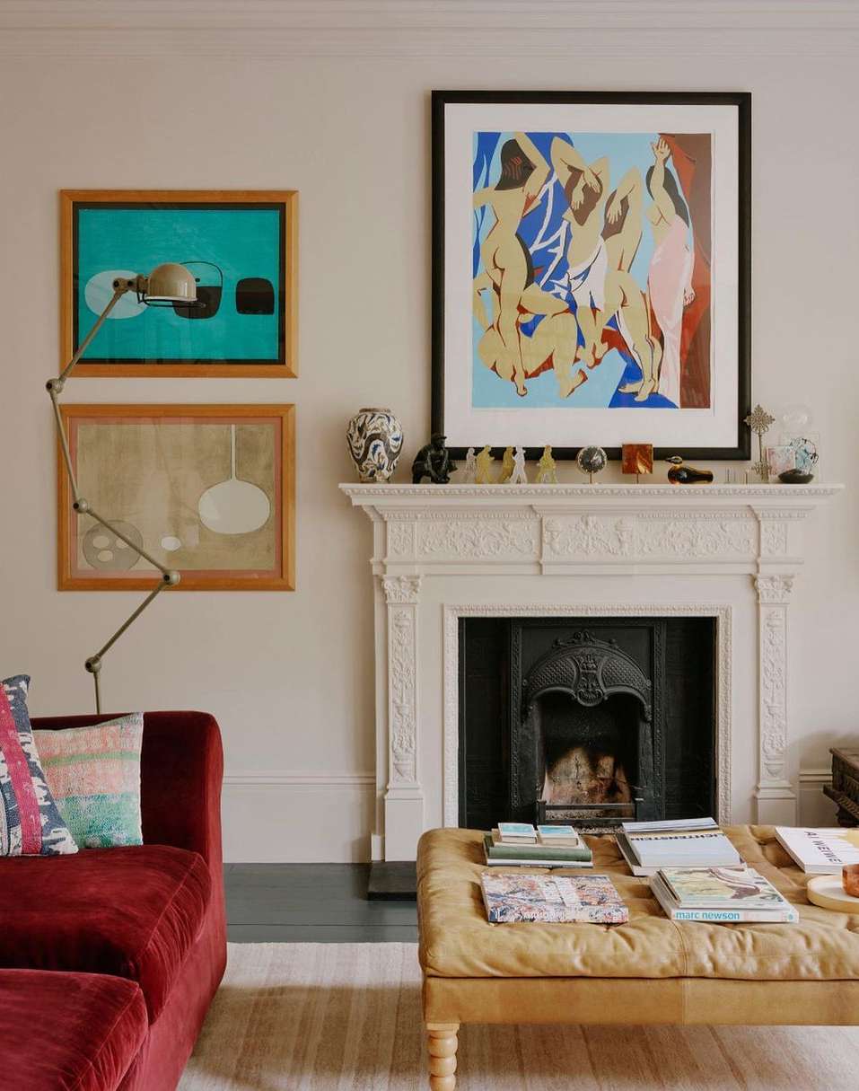 Interior living room featuring a velvet sofa, ornate fireplace mantel with framed art, and a tufted coffee table with books.