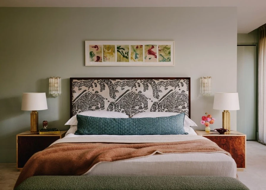 Bedroom interior with a king-sized bed, patterned headboard, and sage green walls. Nightstands flank the bed, each with a table lamp.