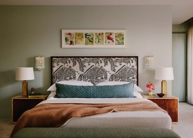 Bedroom interior with a king-sized bed, patterned headboard, and sage green walls. Nightstands flank the bed, each with a table lamp.