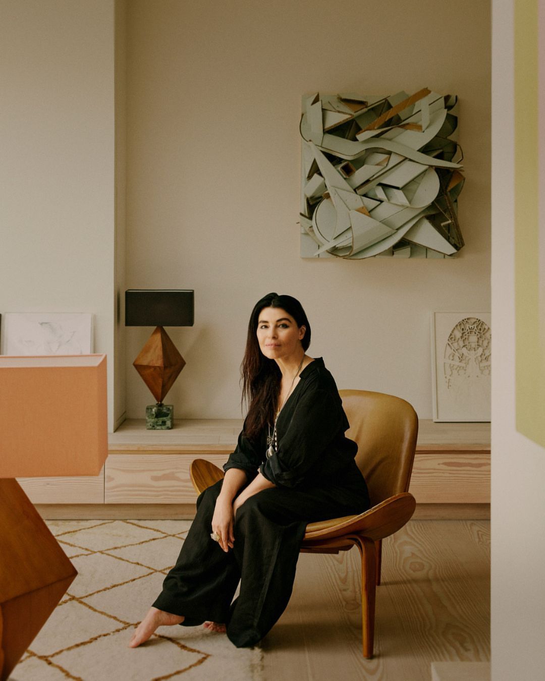 Adult woman in black loungewear sits in modern chair in a home interior with neutral tones, geometric objects, and contemporary art.