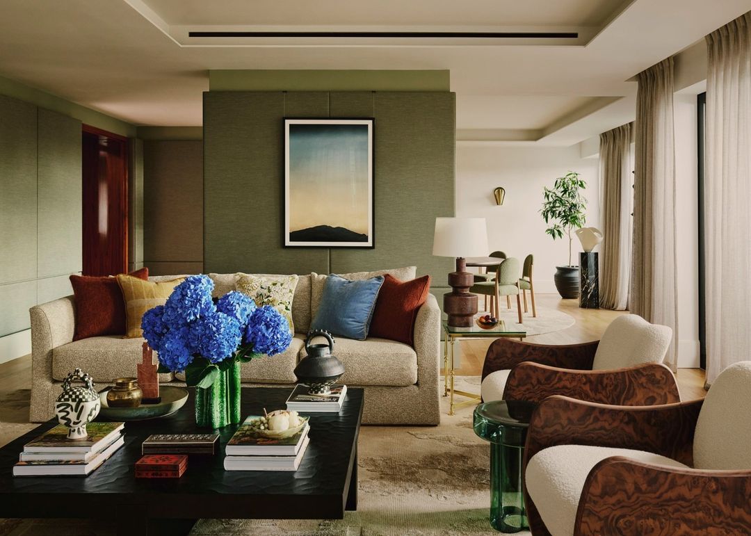 Living room interior showcasing a sofa with pillows, blue hydrangeas in a green vase, a dark coffee table, and two wooden armchairs.