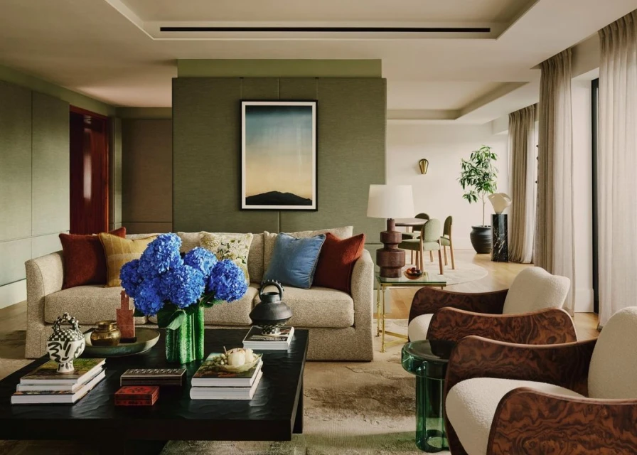 Living room interior showcasing a sofa with pillows, blue hydrangeas in a green vase, a dark coffee table, and two wooden armchairs.