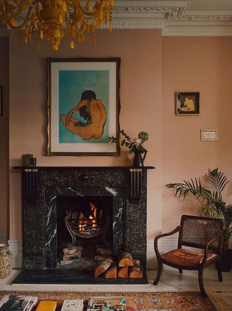 Living room interior featuring a marble fireplace, art prints, a wooden chair, and warm lighting from a chandelier.