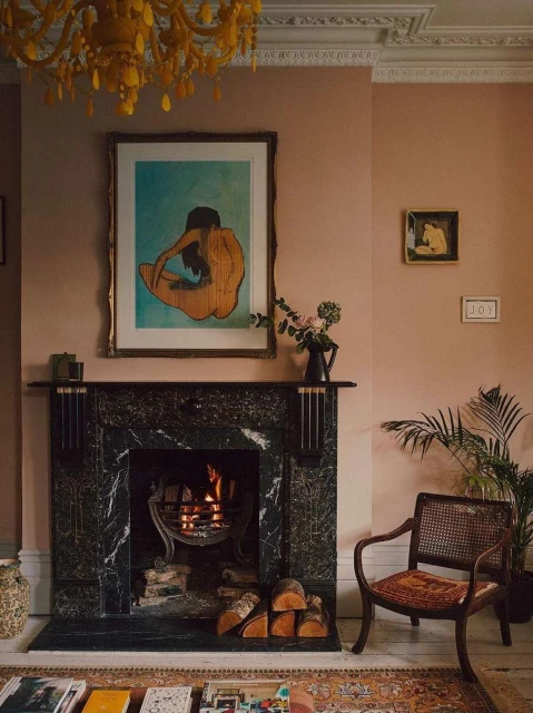 Living room interior featuring a marble fireplace, art prints, a wooden chair, and warm lighting from a chandelier.