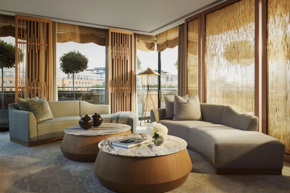 Contemporary living room showcasing beige sofas, round marble-topped coffee tables, and natural light filtering through decorative window screens.