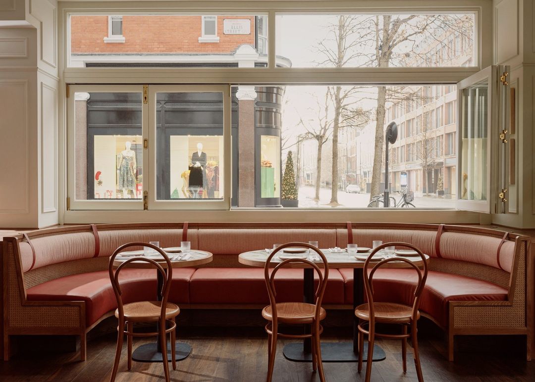 Interior view of an empty restaurant featuring booths, tables set with glassware, and a street view visible through large windows.