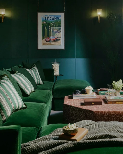 Living room interior featuring a green velvet sectional sofa, patterned pillows, a dark green wall, and artwork, creating a cozy atmosphere.