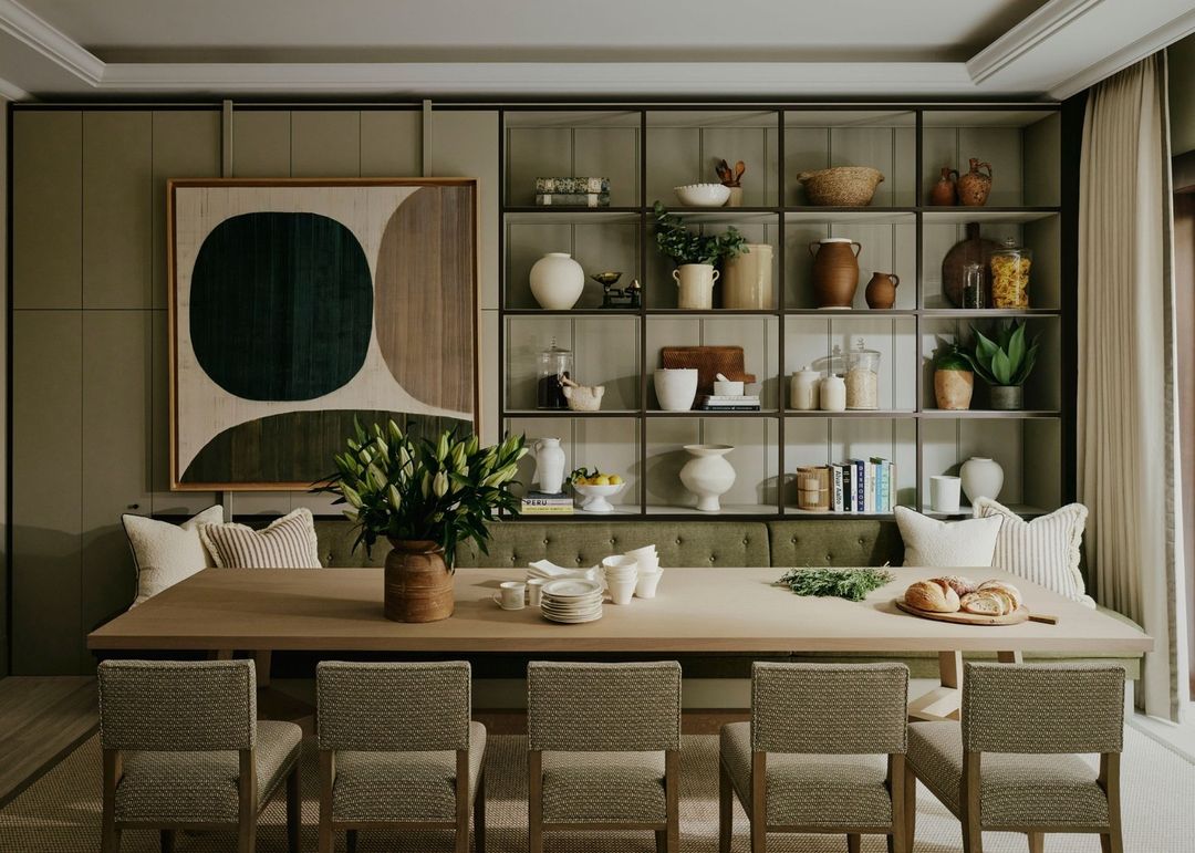 Interior of a dining room featuring a large wooden table with chairs, a vase of white lilies, and built-in shelving filled with dishware.
