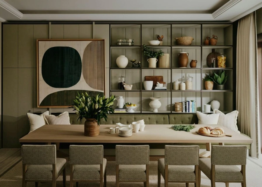 Interior of a dining room featuring a large wooden table with chairs, a vase of white lilies, and built-in shelving filled with dishware.