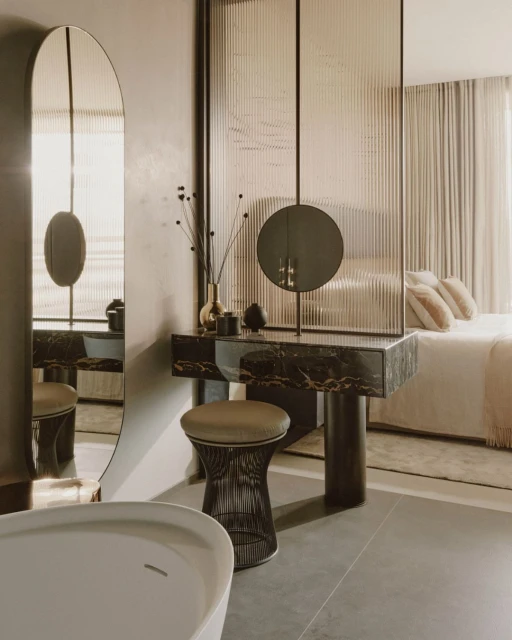 Modern bathroom interior features a vanity with a round mirror, stool, and white bathtub in a stylish home setting.
