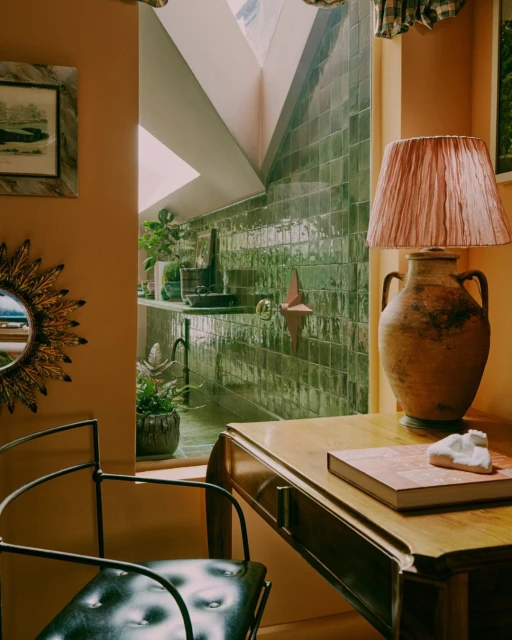 Interior design with an antique desk, a tiled bathroom sink area, and a sunburst mirror; warm neutral and green tones throughout.