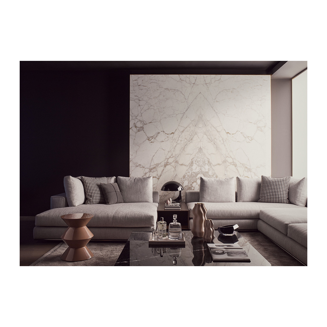 Modern living room interior with sectional sofa, marble accent wall, coffee table with decor, and neutral color palette in a well-lit space.